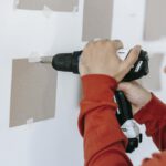 Close-up of hands using a drill on wall in home improvement setting.